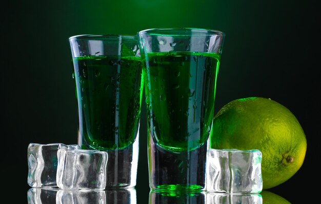 Two glasses of absinthe lime and ice on green background