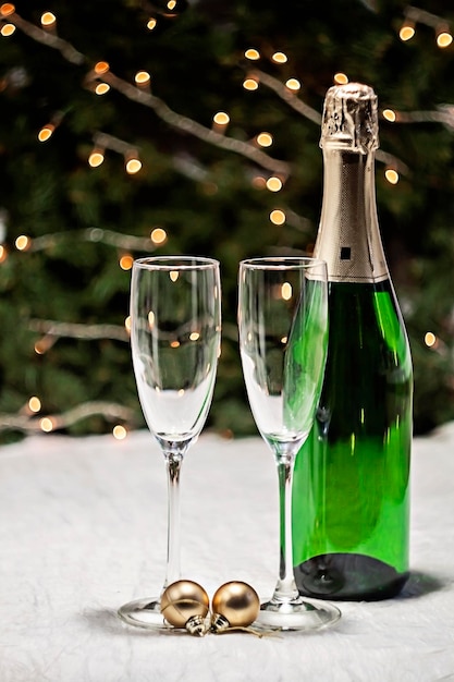 Two glasses and a bottle of champagne is on a festive tablecloth on the table against the background of the Christmas tree and lights