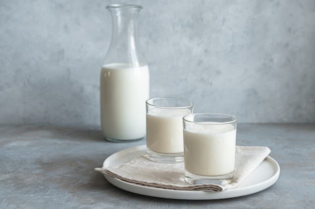 Two glasses and a bottle of fresh milk drink on a gray wall. Lassi, kefir, yogurt. Side view, horizontal.