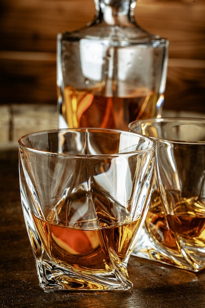 Two glasses of brandy or cognac and bottle on the wooden table