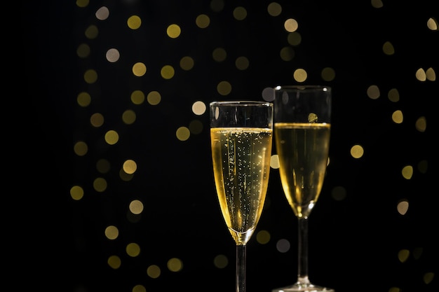 two glasses of bubbling champagne with golden christmas lights in the background close up shot
