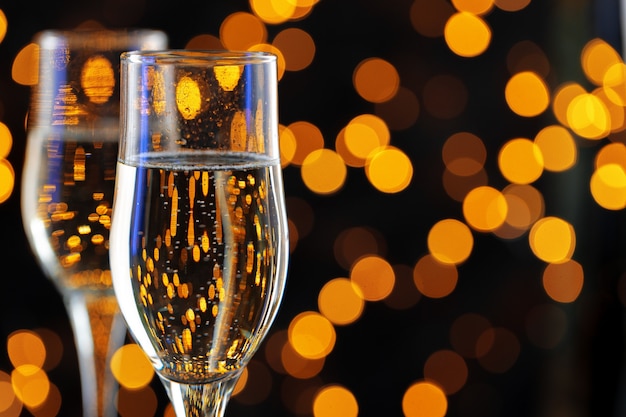 two glasses of champagne against shiny bokeh lights background