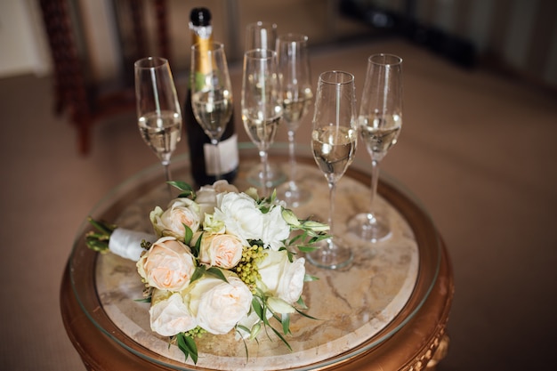 Two glasses of champagne and a beautiful wedding bouquet of buttercups and white lilac on a white painted wooden board