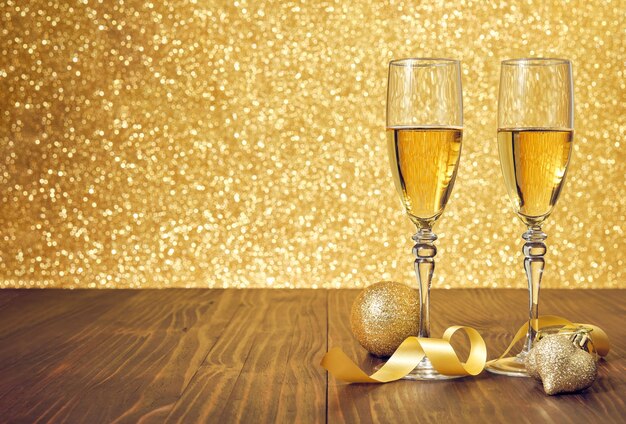 Two glasses of champagne on a brown wooden table with christmas decorations and unfocused gold background