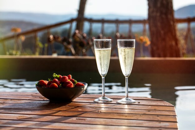 Two glasses of champagne with a plate of strawberries in a pool side terrace