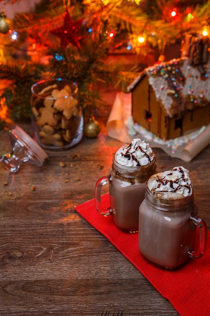 Two glasses of cocoa with whipped cream and chocolate syrup on wooden table