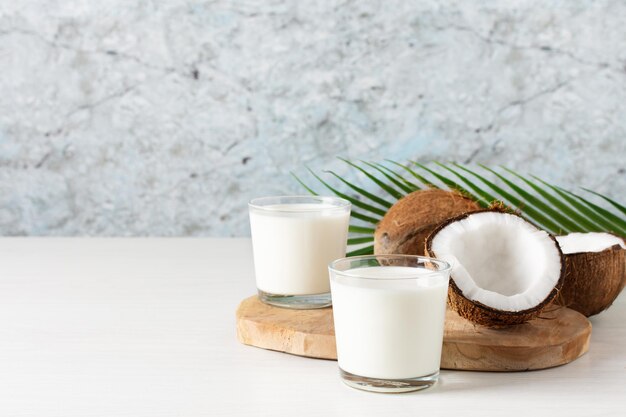 흰색 나무 테이블에 코코넛 반쪽을 넣은 코코넛 비건 우유 두 잔