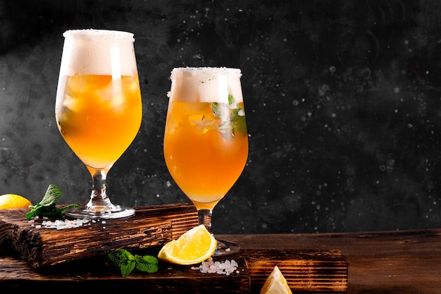 Two glasses of cold beer with lemon and mint traditional latin american drink michelada on dark