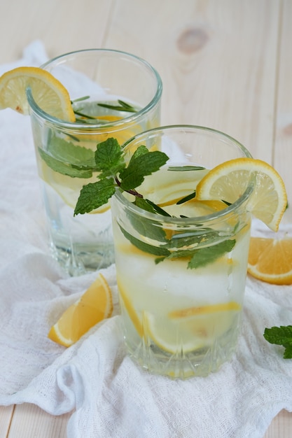 Two glasses of cool lemonade with lemon and mint on a white napkin