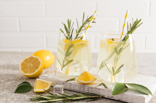 Two glasses of delicious homemade lemonade on a wooden board against a white brick wall and fruit