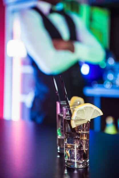 Two glasses of gin on bar counter and bartender leaning 