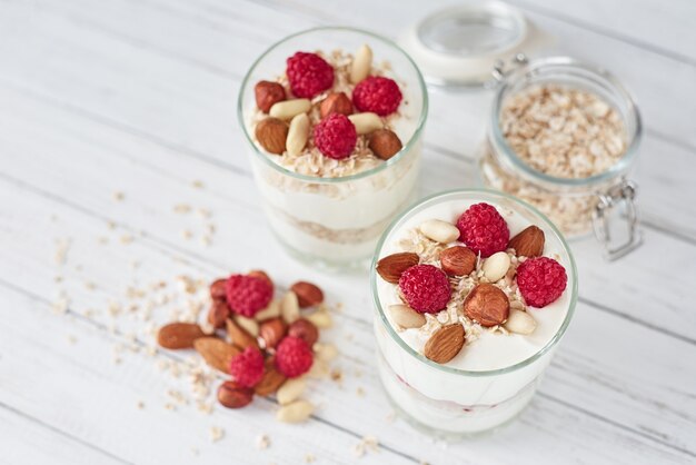 Two glasses of greek yogurt granola with raspberries, oatmeal flakes and nuts 