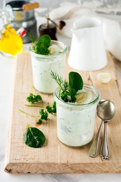 Two glasses of healthy yogurt with a variety of herbs, spinach, dill, onions, parsley and quail eggs. The concept of a healthy vegetarian breakfast. Selective focus.