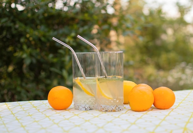 Two glasses of homemade lemonade in background of summer green garden Chilled freshly prepared lemonade and fruit on table in fresh air