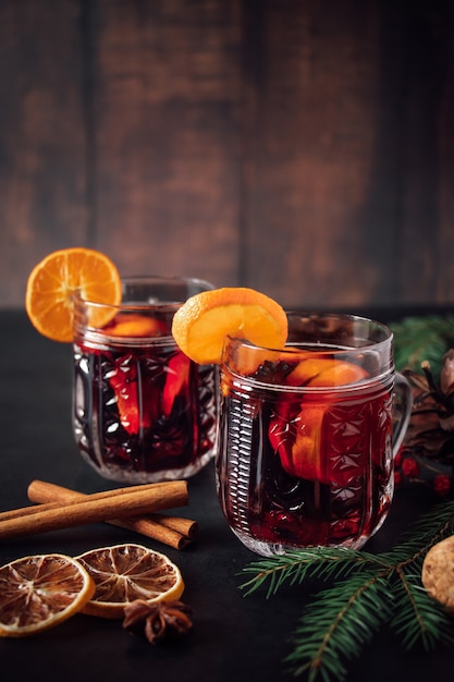 Two glasses of hot mulled wine with fruits and spices on a dark\
background. winter warming holiday drink.