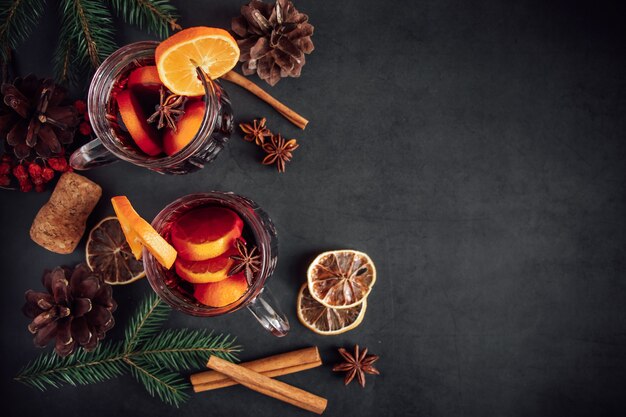 Two glasses of hot mulled wine with fruits and spices on a dark background. Winter warming holiday drink.