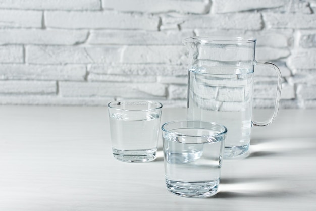 Two glasses and a jug with water on white wooden background Refreshment drinking water