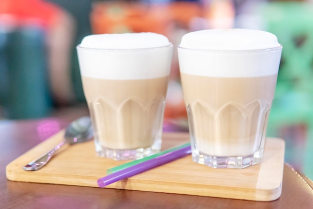 two glasses of latte with froth on a wooden plate on the table