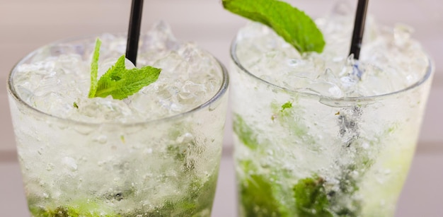 Foto due bicchieri di limonata o cocktail mojito con limone e menta fresca bevanda rinfrescante o bevanda all'aperto acqua disintossicante fredda con spazio per copiare ghiaccio e paglia