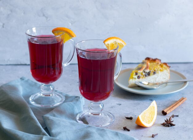 Two glasses of mulled wine, a piece of pie, spices on a light background