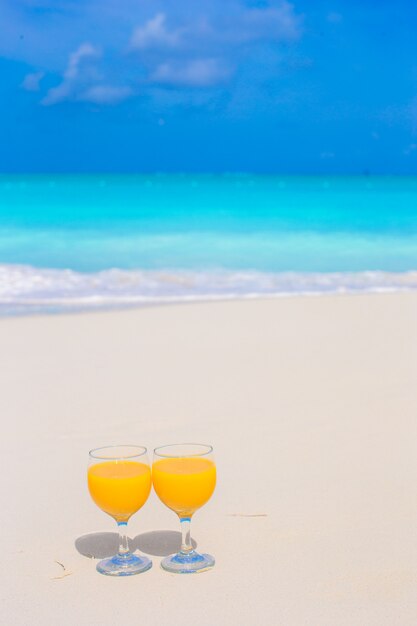 Two glasses of orange juice on tropical white beach