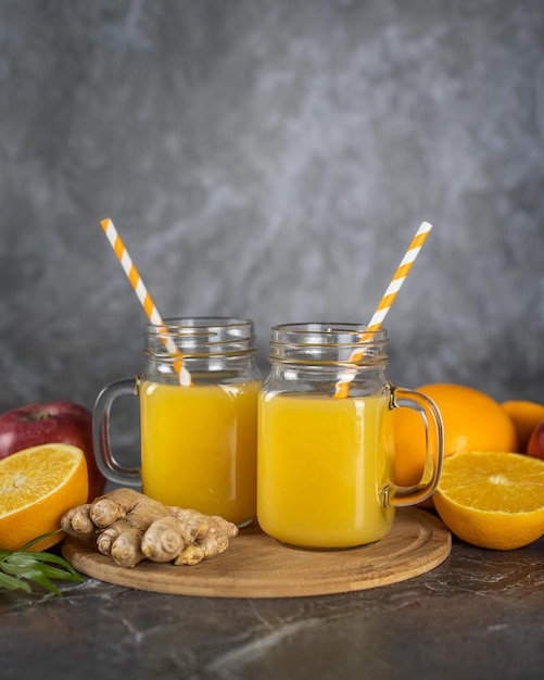 Two glasses of orange juice with oranges and ginger on a wooden cutting board.