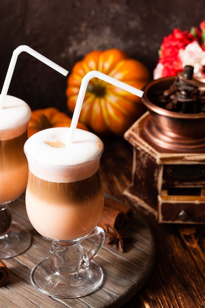 Two glasses pumpkin spicy latte with whipped cream and cinnamon on a wooden stand