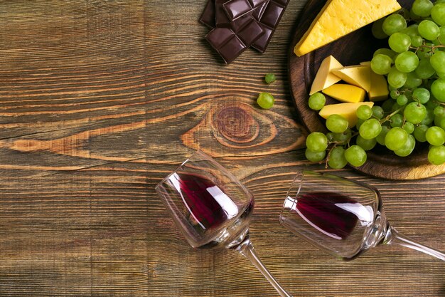 Two glasses of red wine, cheese, green grapes and chocolate, top view. Copy space. Still life. Flat lay