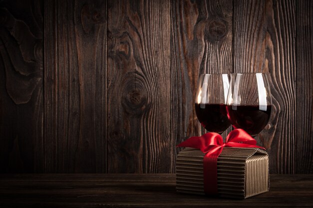 Due bicchieri di vino rosso e confezione regalo con fiocco su fondo di legno scuro