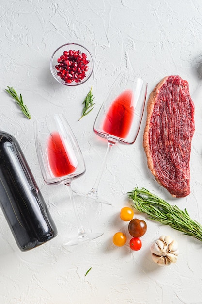 Due bicchieri di vino rosso vicino alla bottiglia e bistecche di manzo su sfondo bianco cemento vista dall'alto