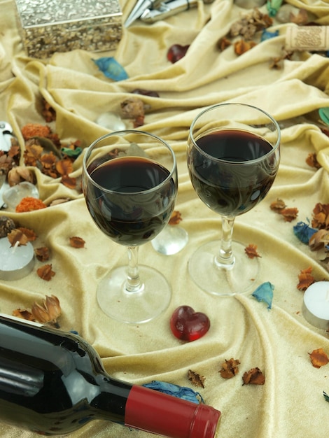 Two glasses of red wine sit on a table with a colorful cloth with a heart shaped decoration.