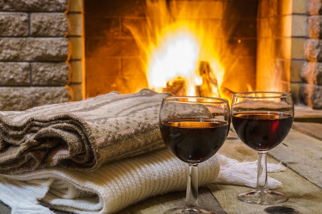 Due bicchieri di vino rosso e cose di lana vicino al caminetto, in casa di campagna, inverno