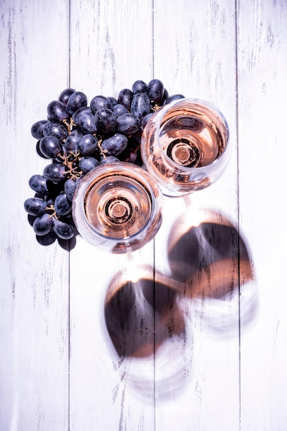 Due bicchieri di vino rosato con uva su un tavolo di legno chiaro