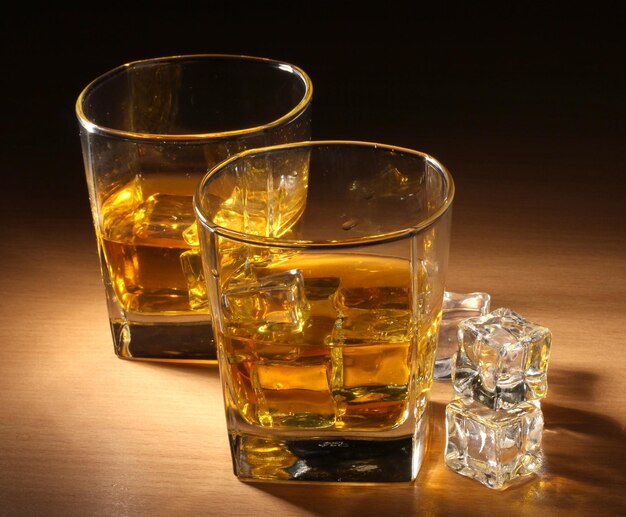 Two glasses of scotch whiskey and ice on wooden table