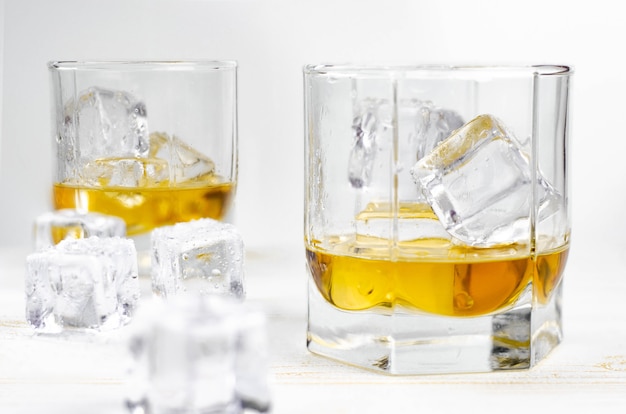 Two glasses of scotch whiskey with ice cubes on white