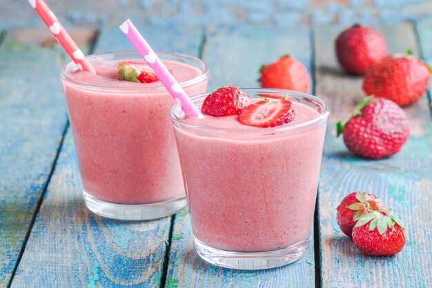 Two glasses of strawberry smoothie with straws on a wooden table