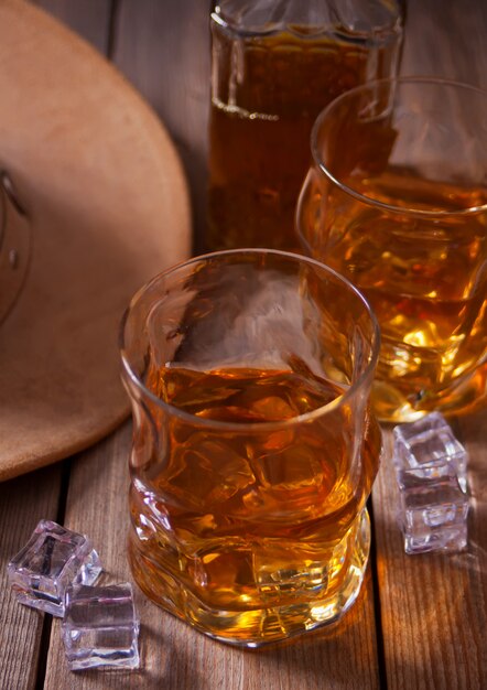 Two glasses of whiskey and cowboy hat on the wooden table.