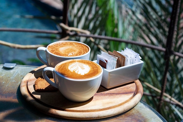 Two glasses white coffee cup with cappuccino in morning on on wooden table with latte art Mug of coffee on a wooden tray Ceramic cup of coffee on round wooden cutting board on color background