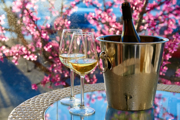 Два бокала белого холодного вина на стеклянный стол на фоне моря и цветов.