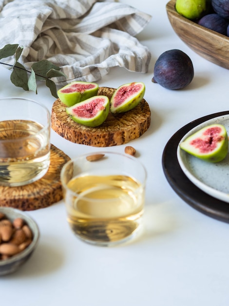 Due bicchieri di vino bianco, fichi e mandorle su uno sfondo bianco.