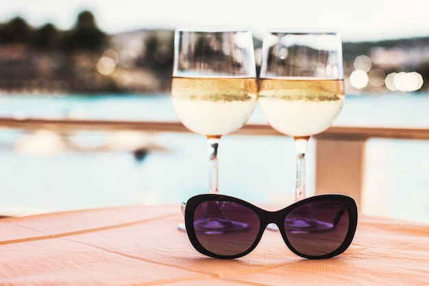 Two glasses of white wine and sunglasses on the table at beach\
cafe with sea view