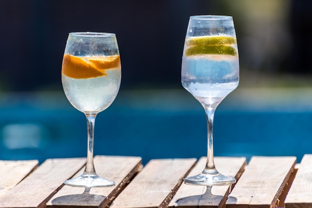 Two glasses of wine next to each other with a blue pool in the background.