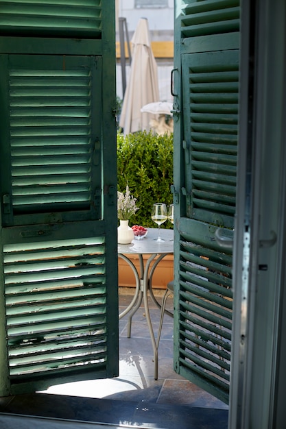 Two glasses of wine, fresh berries on a table on the balcony, view through open shutters