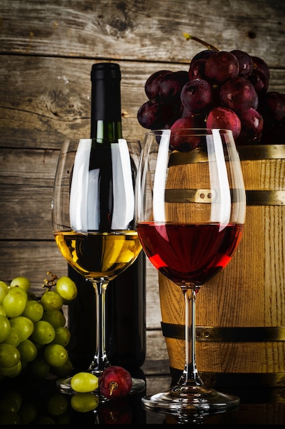 Two glasses of wine with fresh frash grapes, bottle and barrel in front of old grunge wooden planks