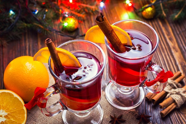 Два стакана зимнего согревающего красного горячего напитка Рождественский глинтвейн на деревянном фоне со специями, апельсиновым ломтиком и палочками корицы