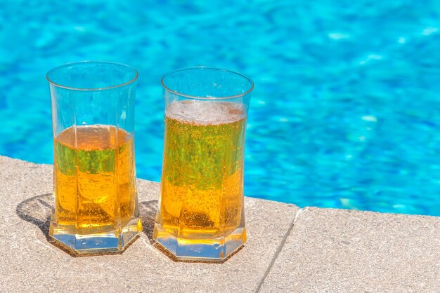 Photo two glasses with beer on the edge of the pool