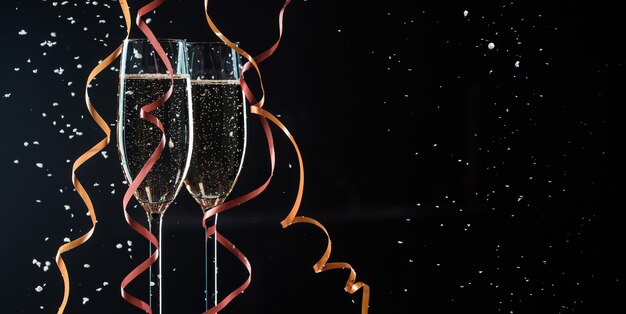 Two glasses with champagne, decorative ribbons and snow flakes closeup. Image on black background with copy space