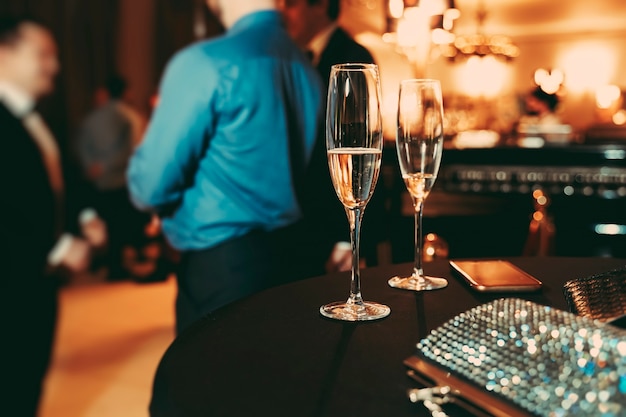 Two glasses with champagne, shiny women's handbag and a phone on the table