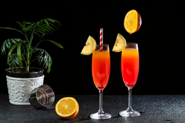 TWO GLASSES WITH COCKTAIL SEX ON THE BEACH, A FLOWER STREAK NEXT TO THE DRINK, ON A DARK BACKGROUND