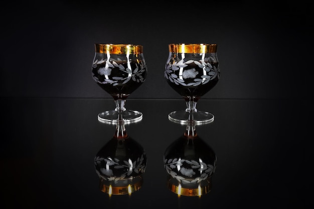 Photo two glasses with dark wine and pattern on mirror black surface